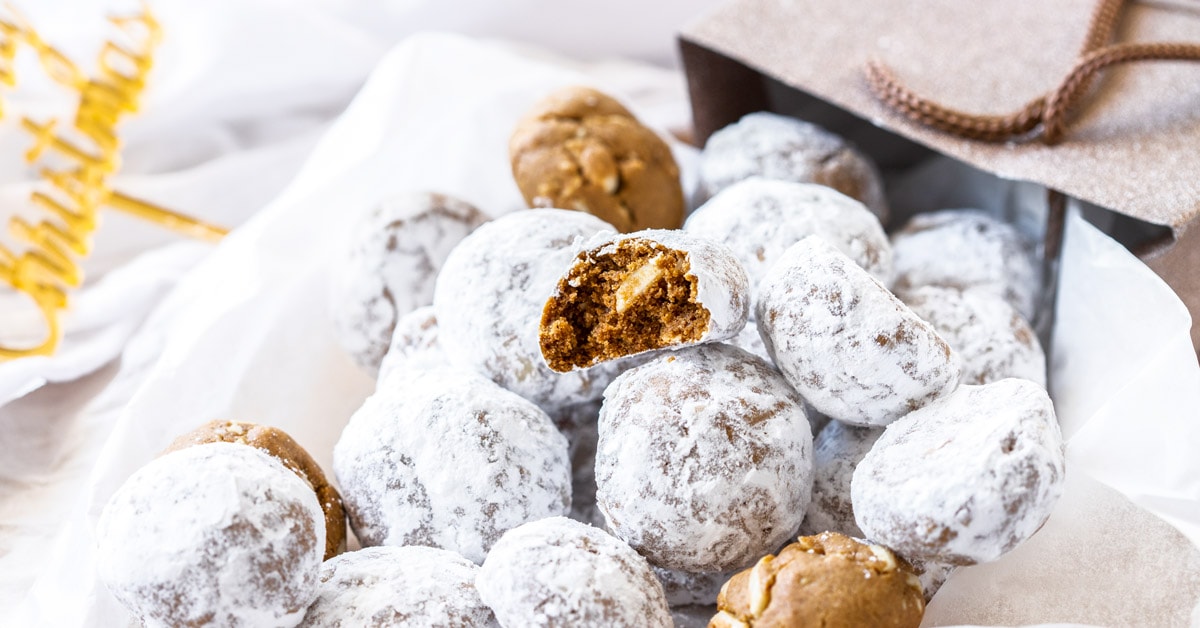 Un montón de galletas de bolas de nieve con sabor a pan de jengibre, cayendo de una bolsa de regalo sobre un papel blanco para hornear