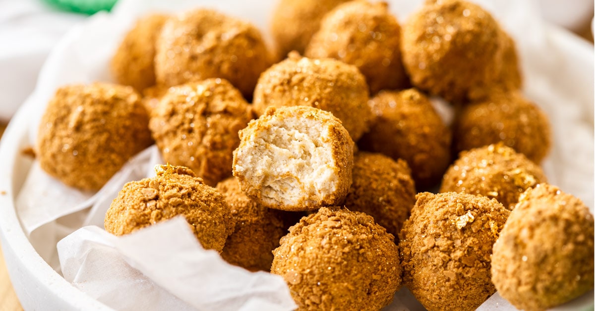 Un plato blanco lleno de bolas de pastel de queso de pan de jengibre con el de arriba con una mordida.