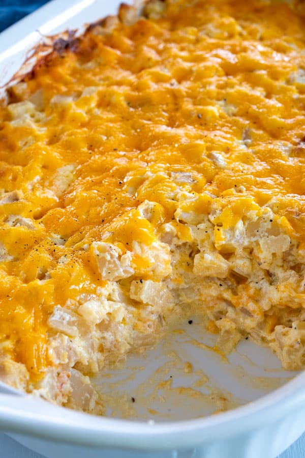 Plato blanco de la cazuela que falta una cucharada de Cheesy Hashbrown Potato Casserole