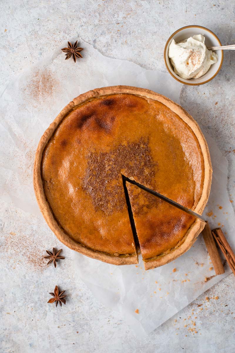 Un pastel de calabaza casero con una rodaja cortada y crema batida a un lado
