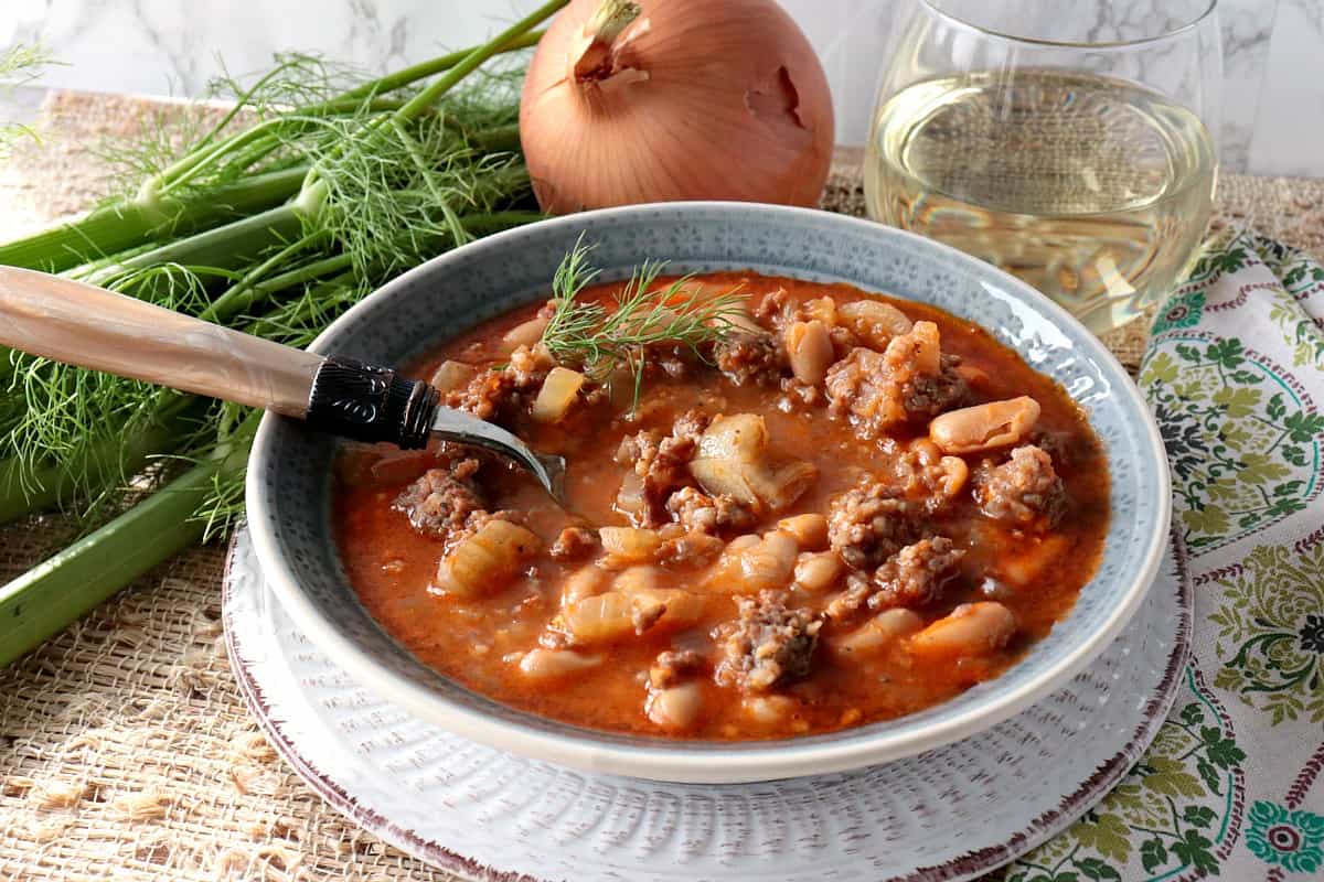 A hearty bowl of White Bean, Fennel & Italian Sausage Soup with Fennel, Onion and a glass of wine.