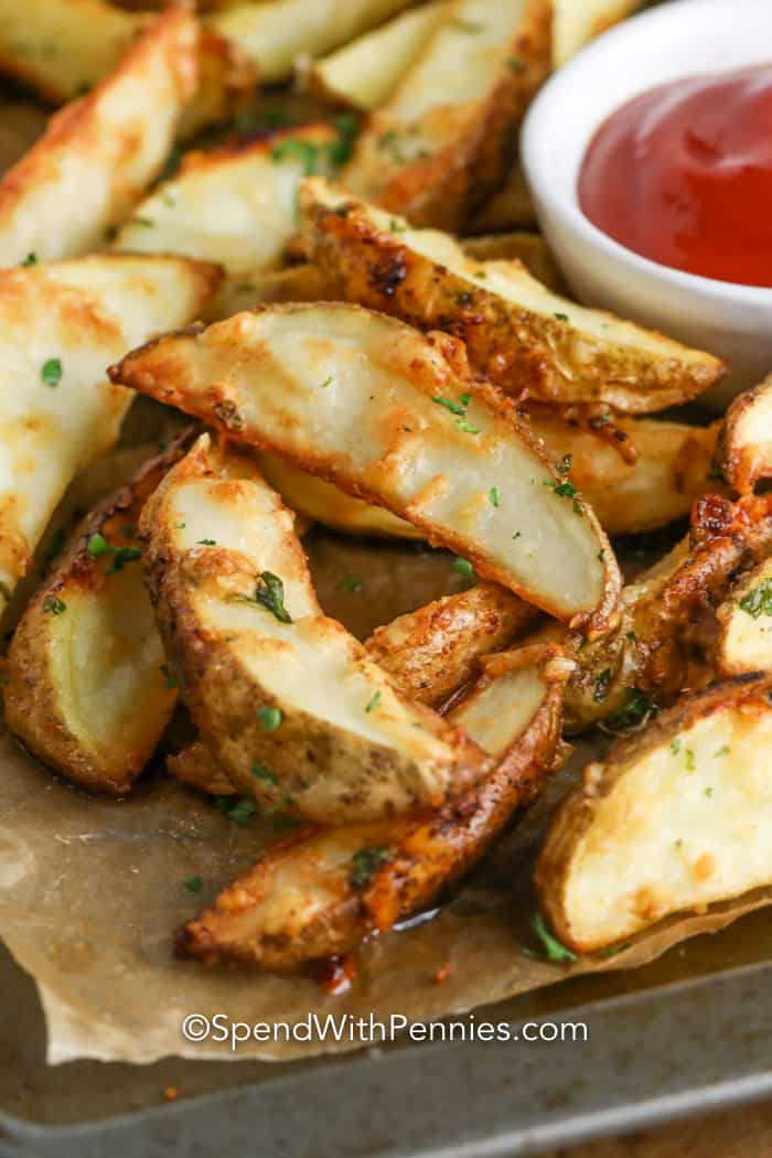 Ciérrese para arriba de las cuñas de patata cocidas crujientes en una bandeja de la hornada con un plato de salsa de tomate.