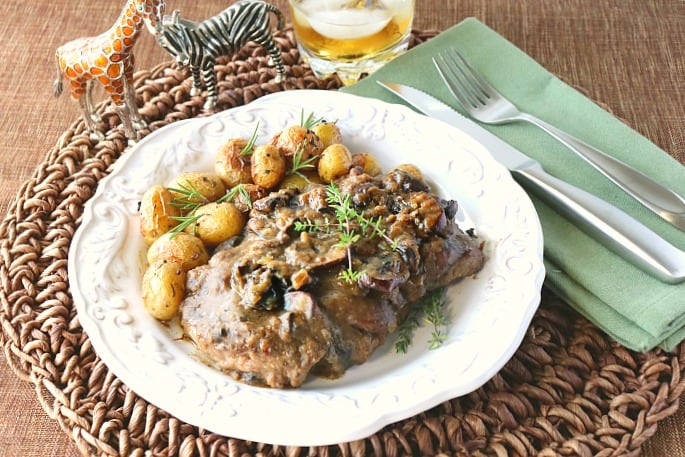 Steak with bourbon mushroom sauce on a white plate with baby potatoes and fresh herbs.