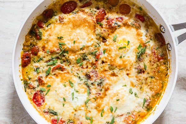 Estos huevos horneados con bruschetta son el complemento perfecto para el brunch de fin de semana. Tomates salteados dulces mezclados con mucho ajo, albahaca y orégano y cubiertos con huevos y queso parmesano. ¡Sirve sobre tostadas y disfruta tu fin de semana!