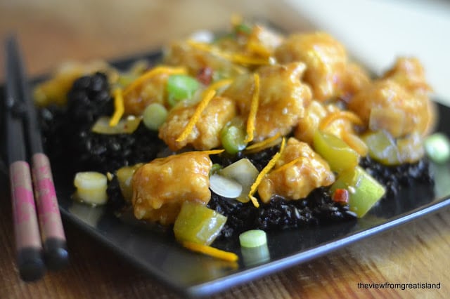 Pollo picante de mandarina con arroz negro en un plato negro con palillos