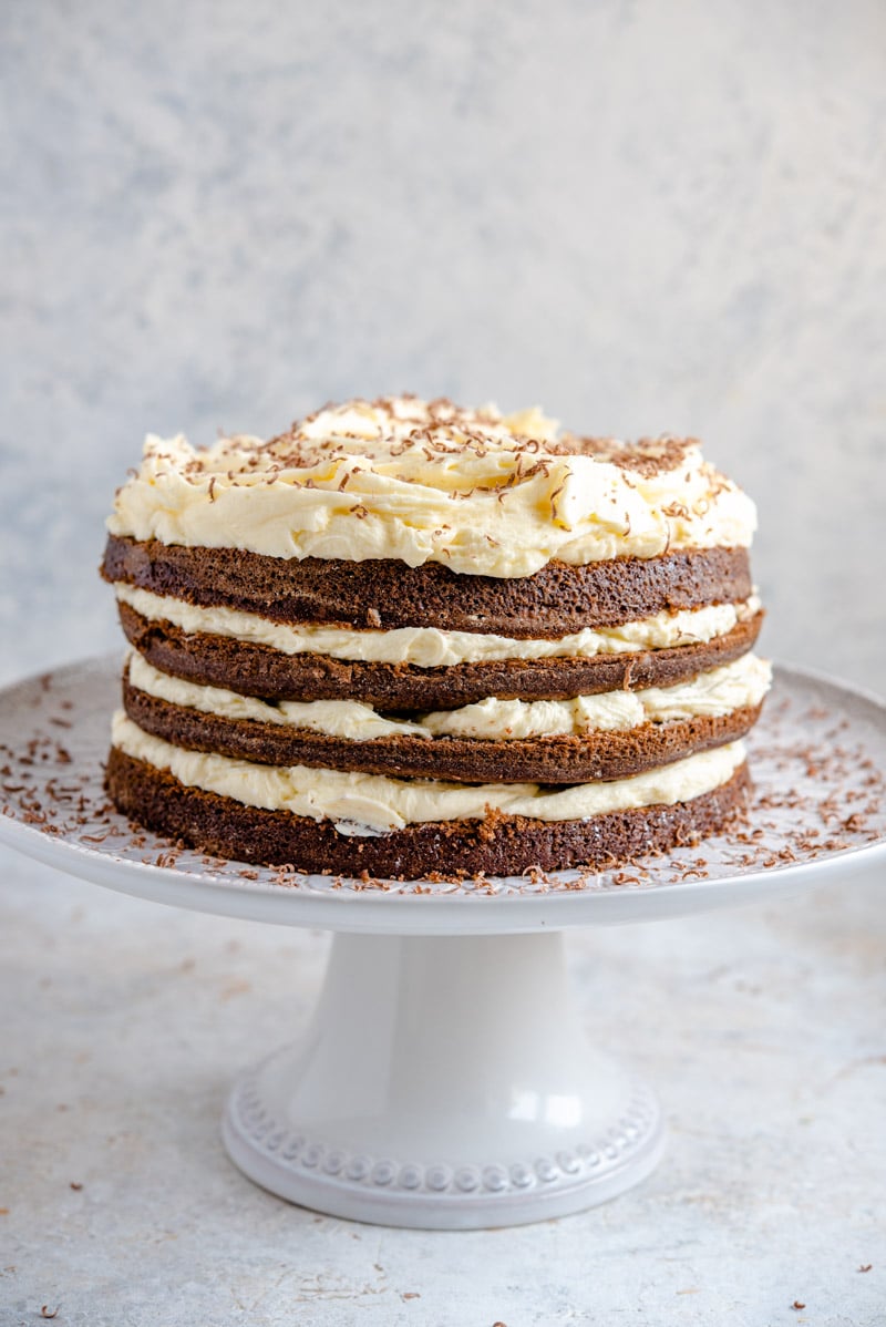 Una foto lateral de un pastel de chocolate de cuatro capas en un soporte de pastel