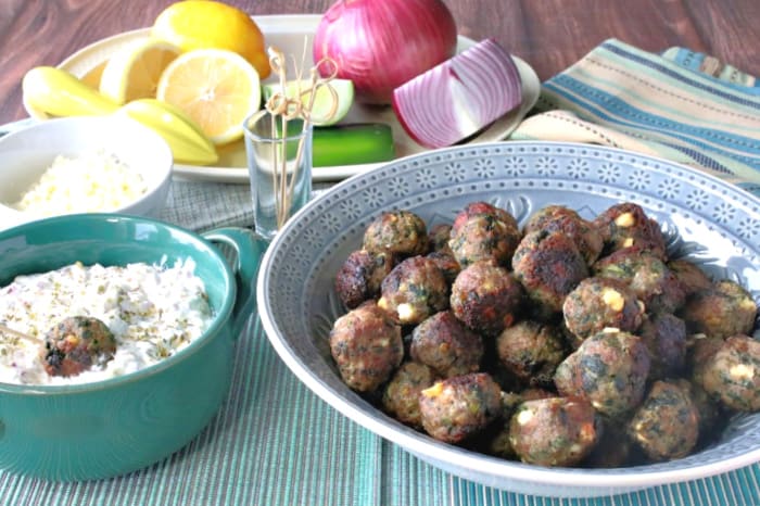 A bowl of Greek meatballs appetizers on the right and a small bowl of tzatziki dipping sauce on the left.