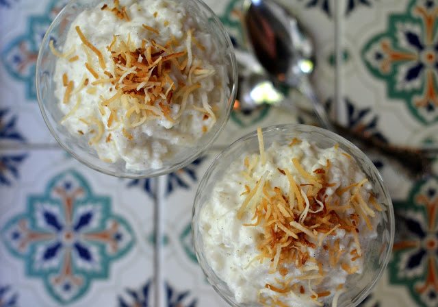 Foto de arriba de dos vasos de bud&iacute;n de arroz cremoso de coco cubierto con coco tostado en una bandeja de azulejos.