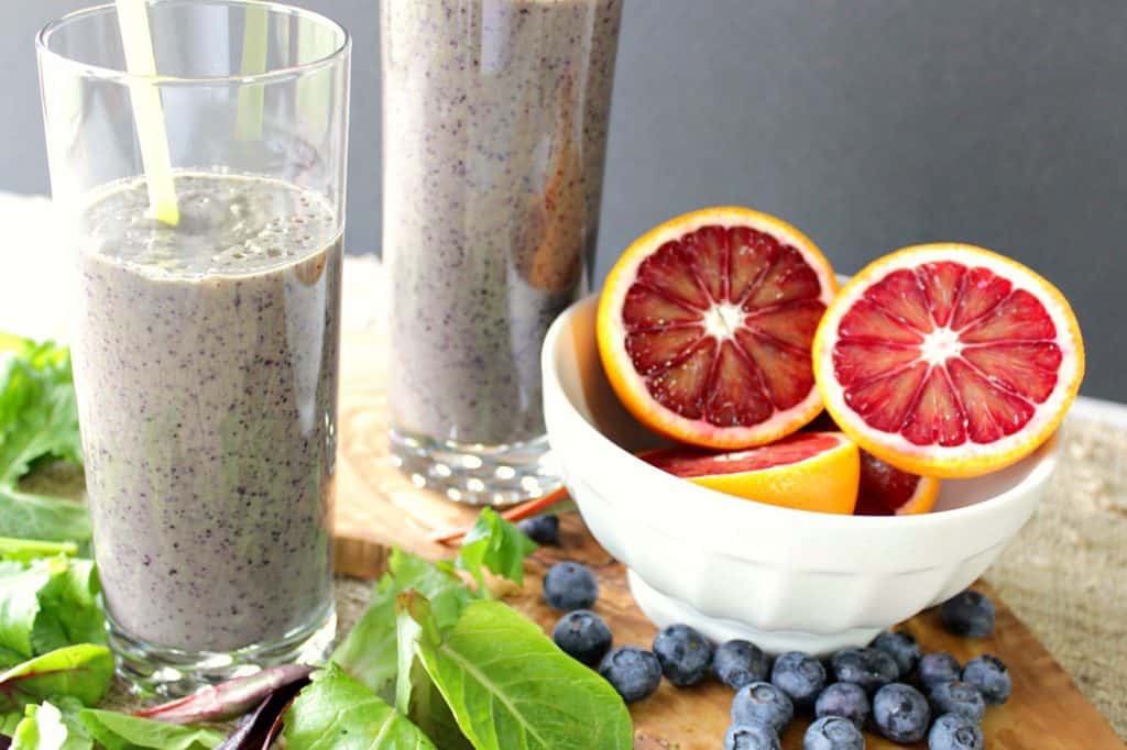 2 batidos de desayuno de naranja y ar&aacute;ndanos con un cuenco de naranjas, ar&aacute;ndanos y lechugas