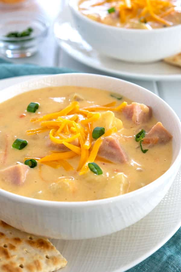 Bowl of cheesy ham and potato soup with cheddar, potatoes and green onions