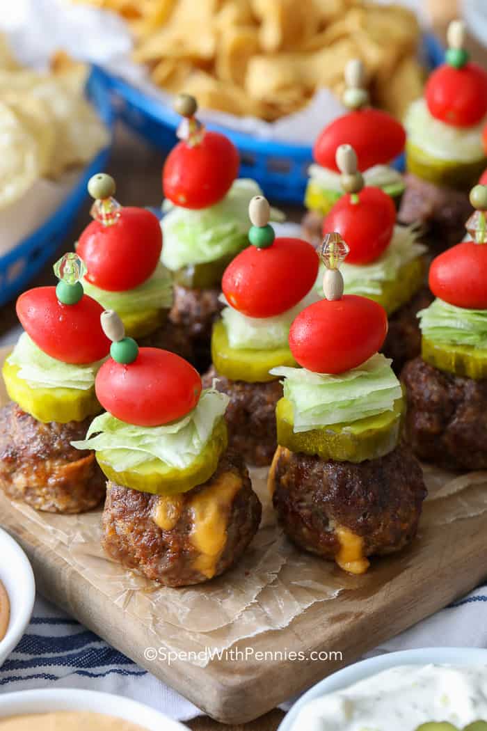 Cerca de alb&oacute;ndigas rellenas de hamburguesa con queso, encurtidos con pepinillos, lechuga y tomates en una tabla para cortar.