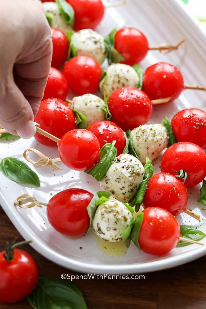 Una brocheta Caprese con tomates cherry, albahaca y mozzarella recogidos de un plato