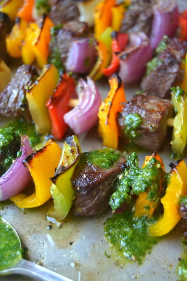 Brochetas de fajita de filete alineadas en una bandeja para hornear rociadas con pesto de cilantro