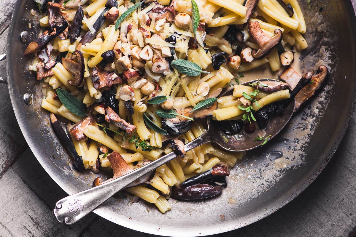 Pasta con champi&ntilde;ones y avellanas en una sart&eacute;n con una cuchara grande