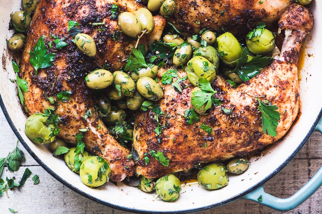 Pollo con aceitunas y hierbas rotas en una sartén