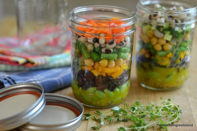 Dos frascos de Mason Jar 7 Bean Salad con tapas y tomillo sobre una superficie de madera.
