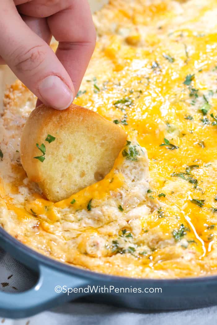 Salsa de cangrejo caliente con queso horneada en una cacerola que se saca con un crostini