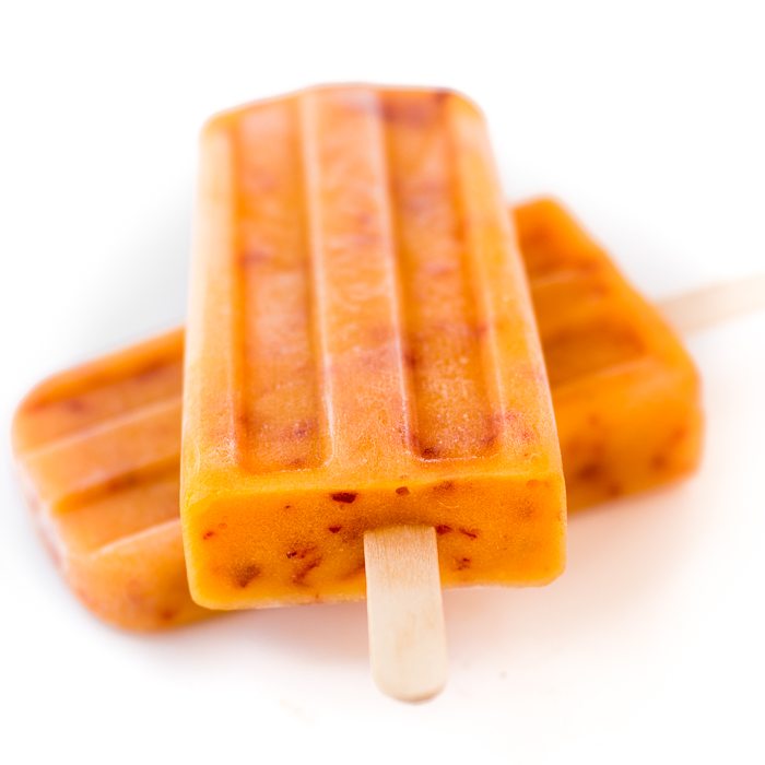 Foto de dos paletas de durazno maduras tendido sobre una superficie blanca.