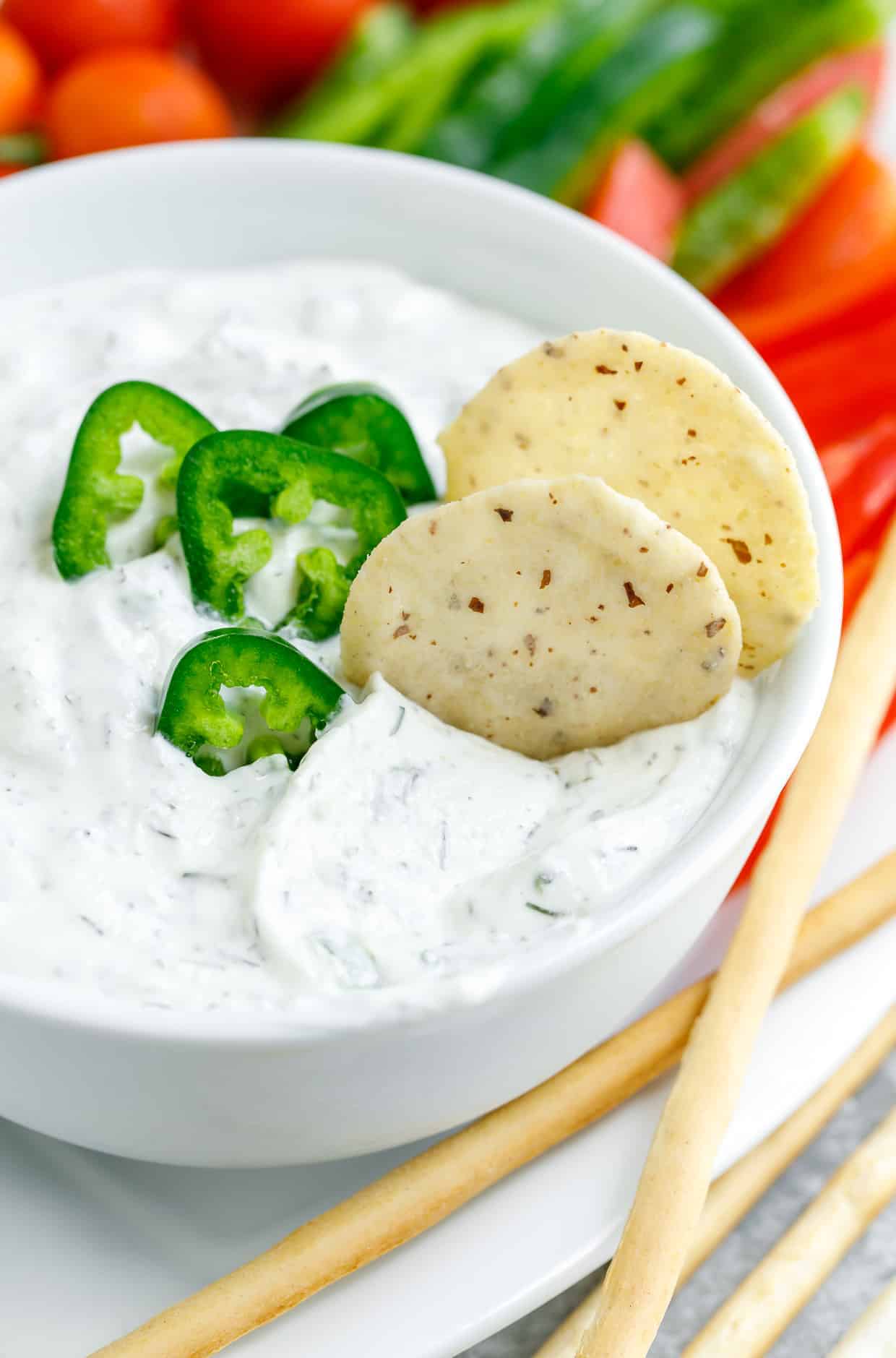 Dip de eneldo picante con jalapeños en un tazón blanco adornado con jalapeños con verduras y dippers