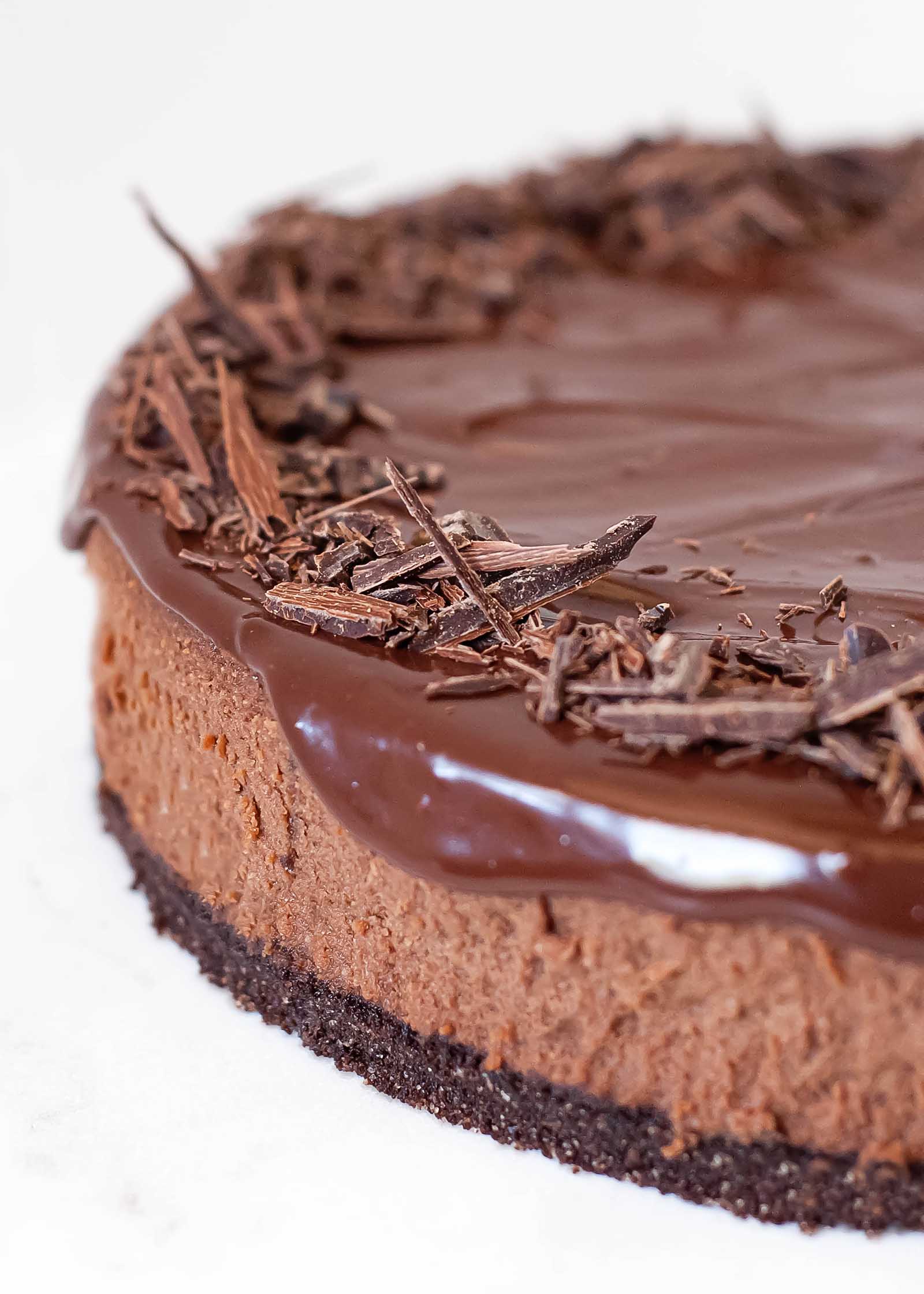 Close up of a chocolate cheeescake with dripping ganache frosting and shards of chocolate on top