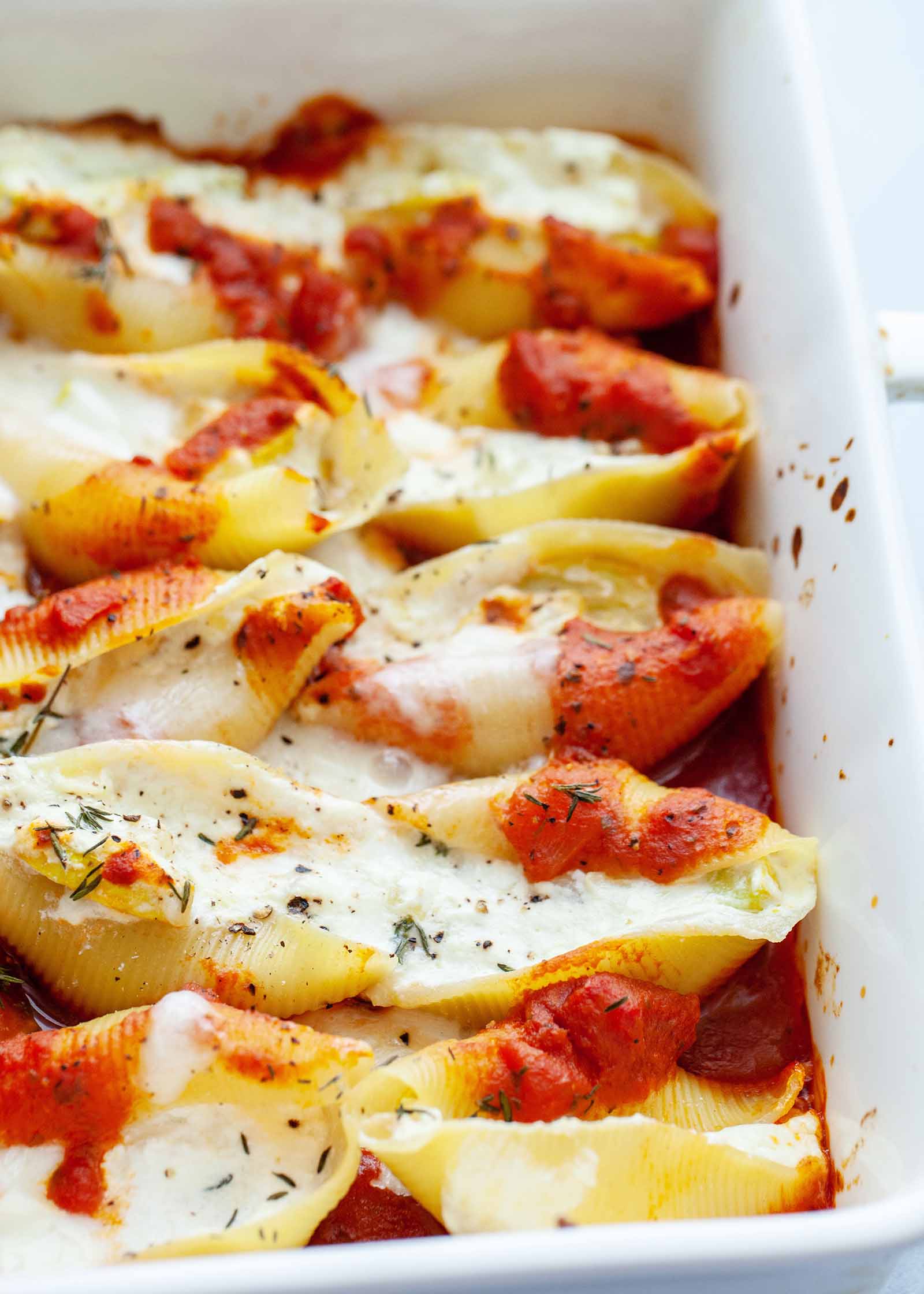 Baked ricotta and squash stuffed shells with sauce in a white baking dish