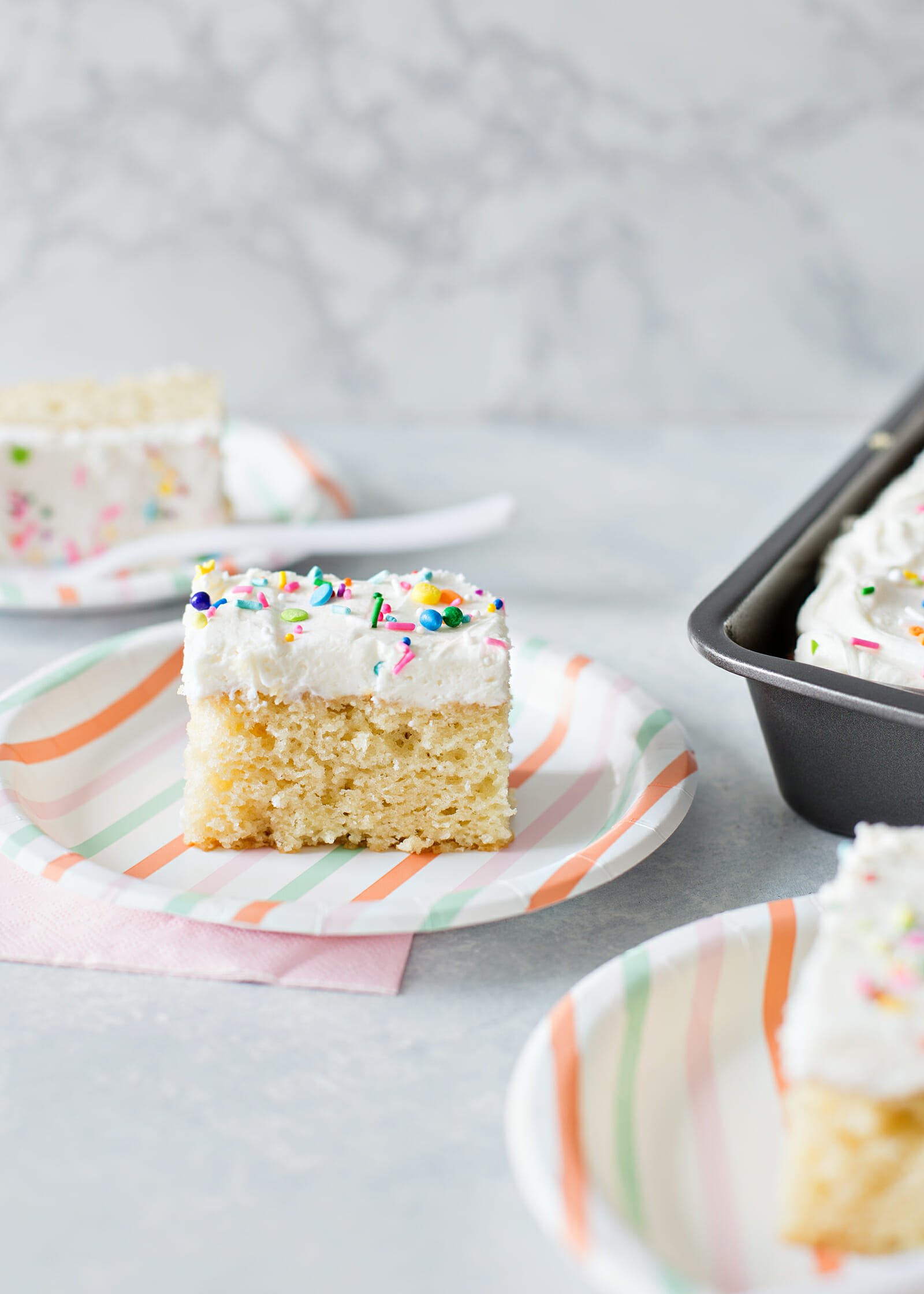 Best Vanilla Cake Recipe - vanilla cake with white frosting and sprinkles on plate.