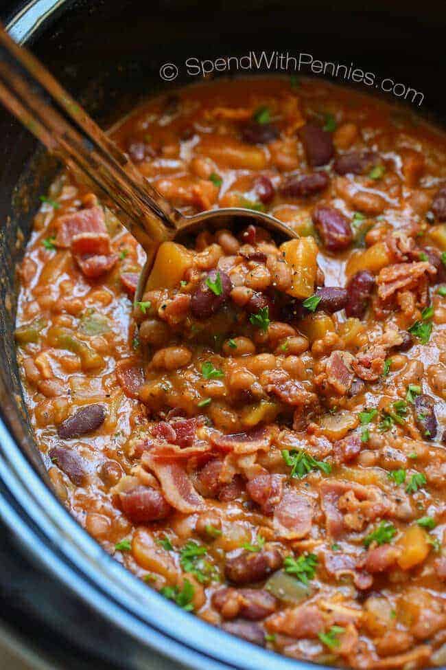 Stirring baked beans in a crockpot with a silver ladle