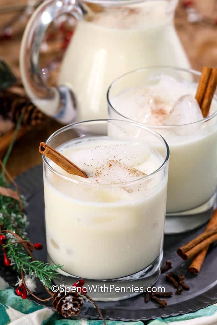 Homemade eggnog into glasses with cinnamon sticks and a pitcher in the background