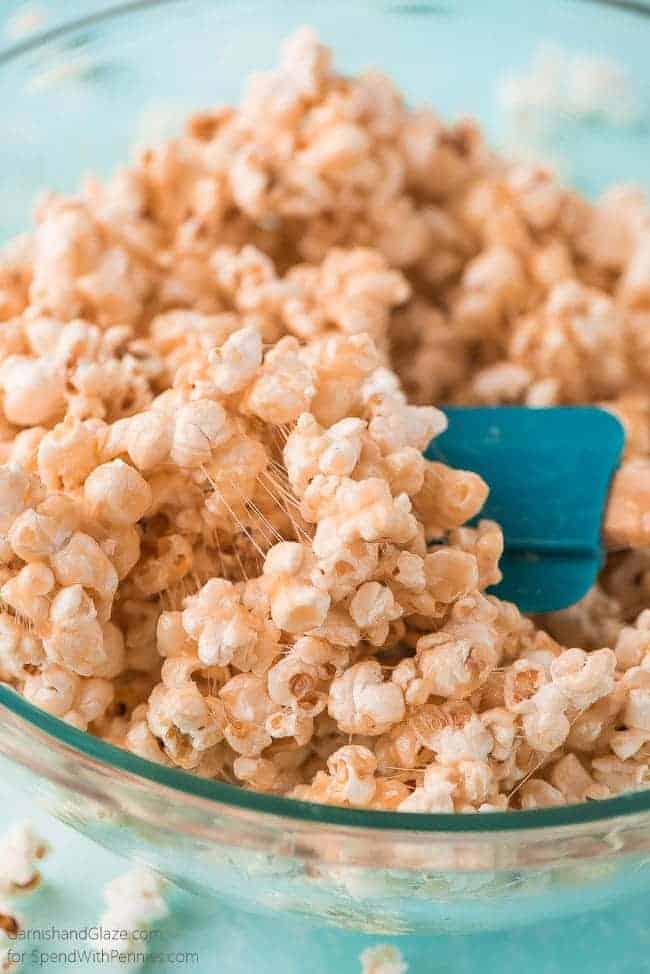 stirring caramel marshmallow popcorn with a spatula in a glass bowl