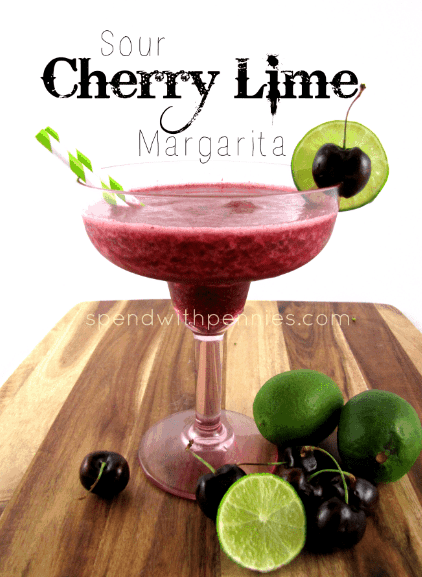 Sour cherry lime margarita in a fancy glass on a wood board with limes and cherries in front