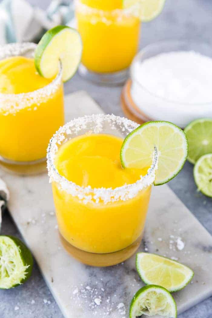 Frozen mango margaritas in round glasses with salt rims and lime wedge with salt and lime on the side