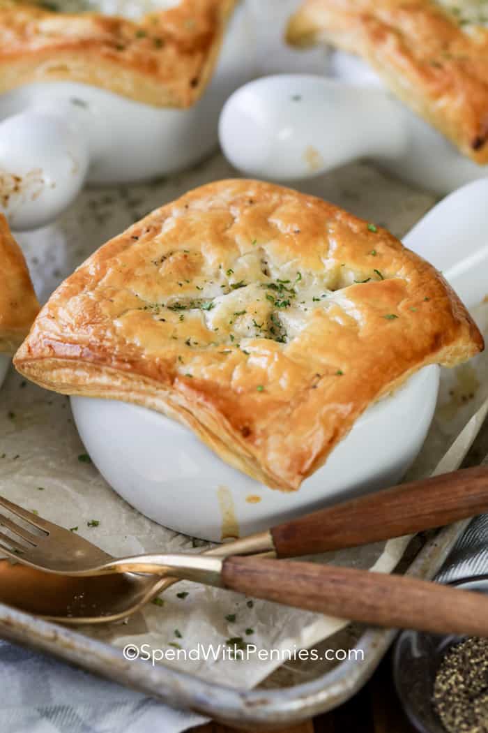 Chicken pot pie in a white dish on a baking sheet with a fork and spoon