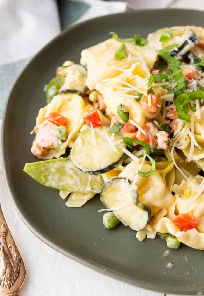Delicious pasta primavera on a green plate with a gold fork