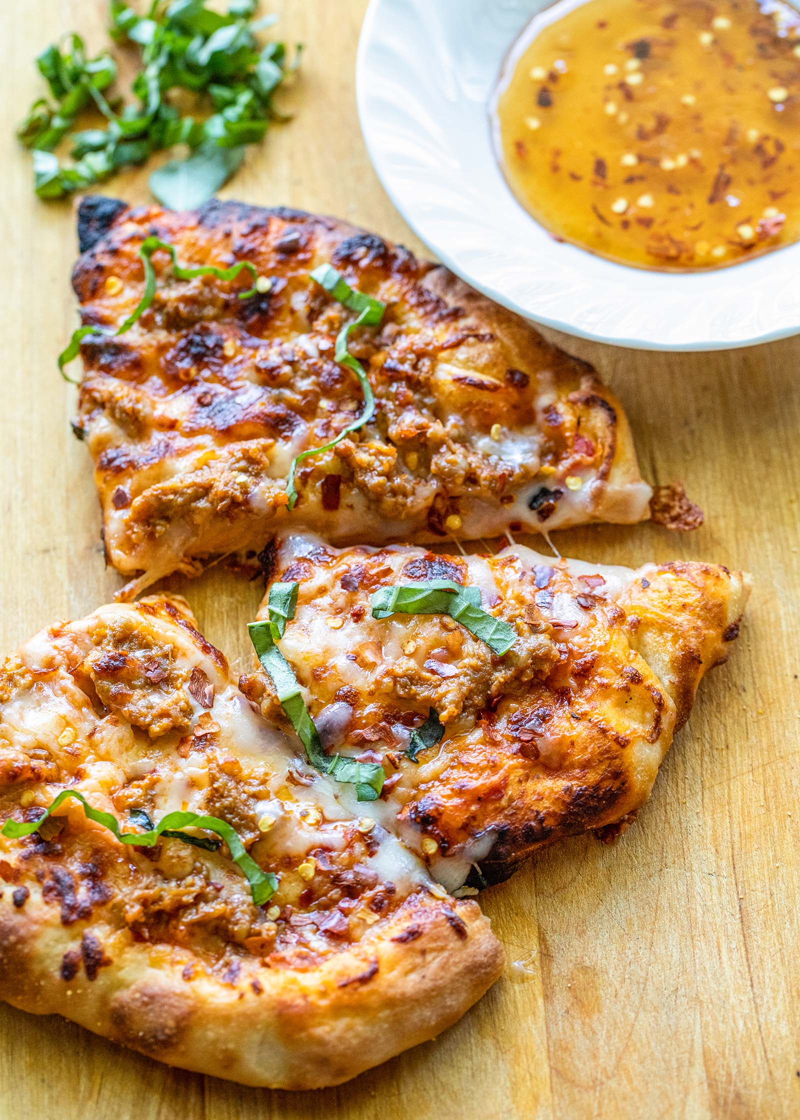 Three pieces of homemade pizza with sausage next to a bowl of hot honey dipping sauce.