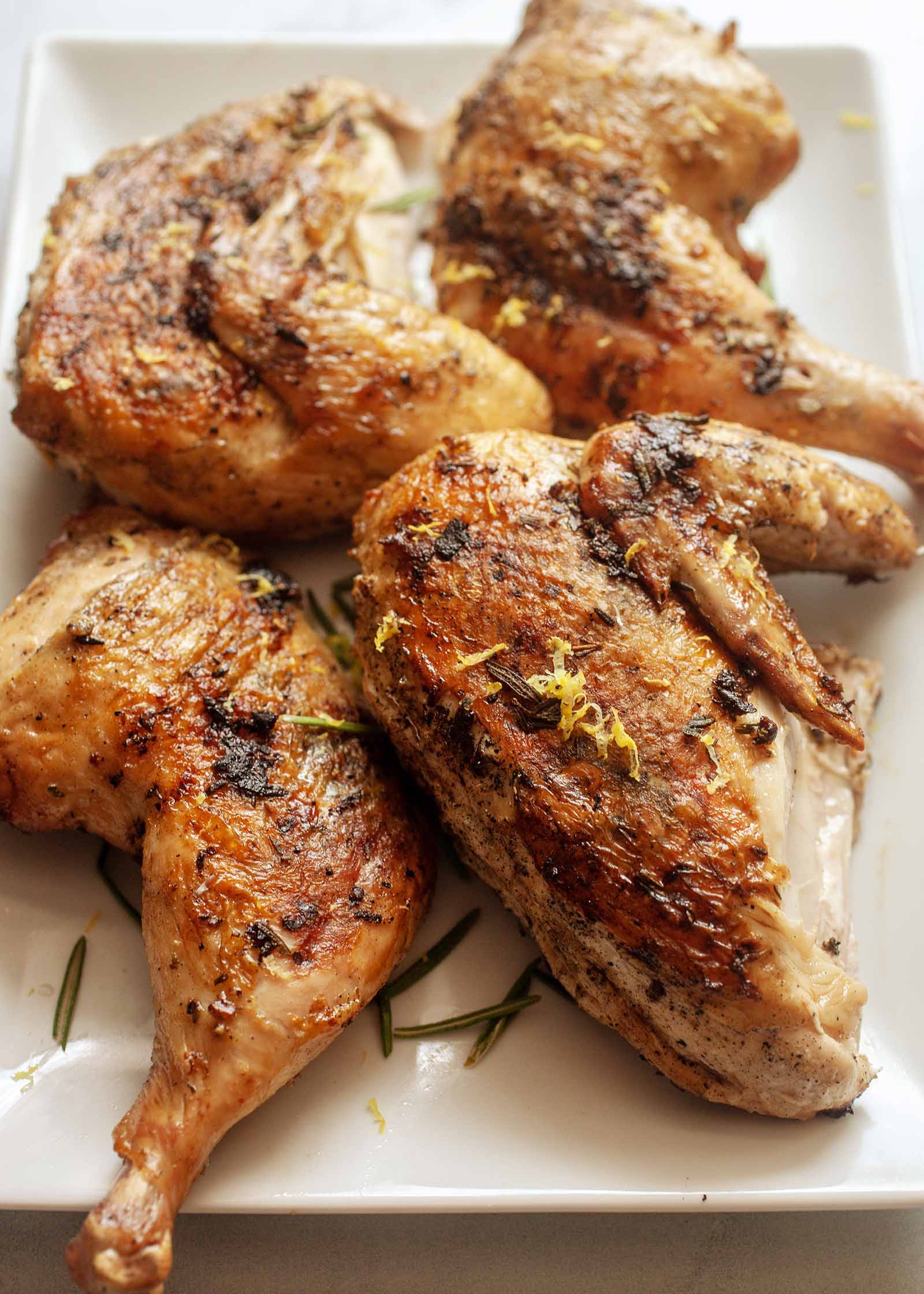 Whole chicken cooked on the grill under a heavy cast iron pan