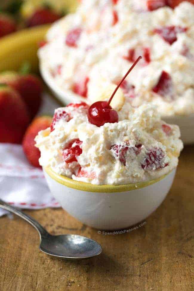 Strawberry Banana Salad serving with a cherry in a small bowl, with the serving dish in the background