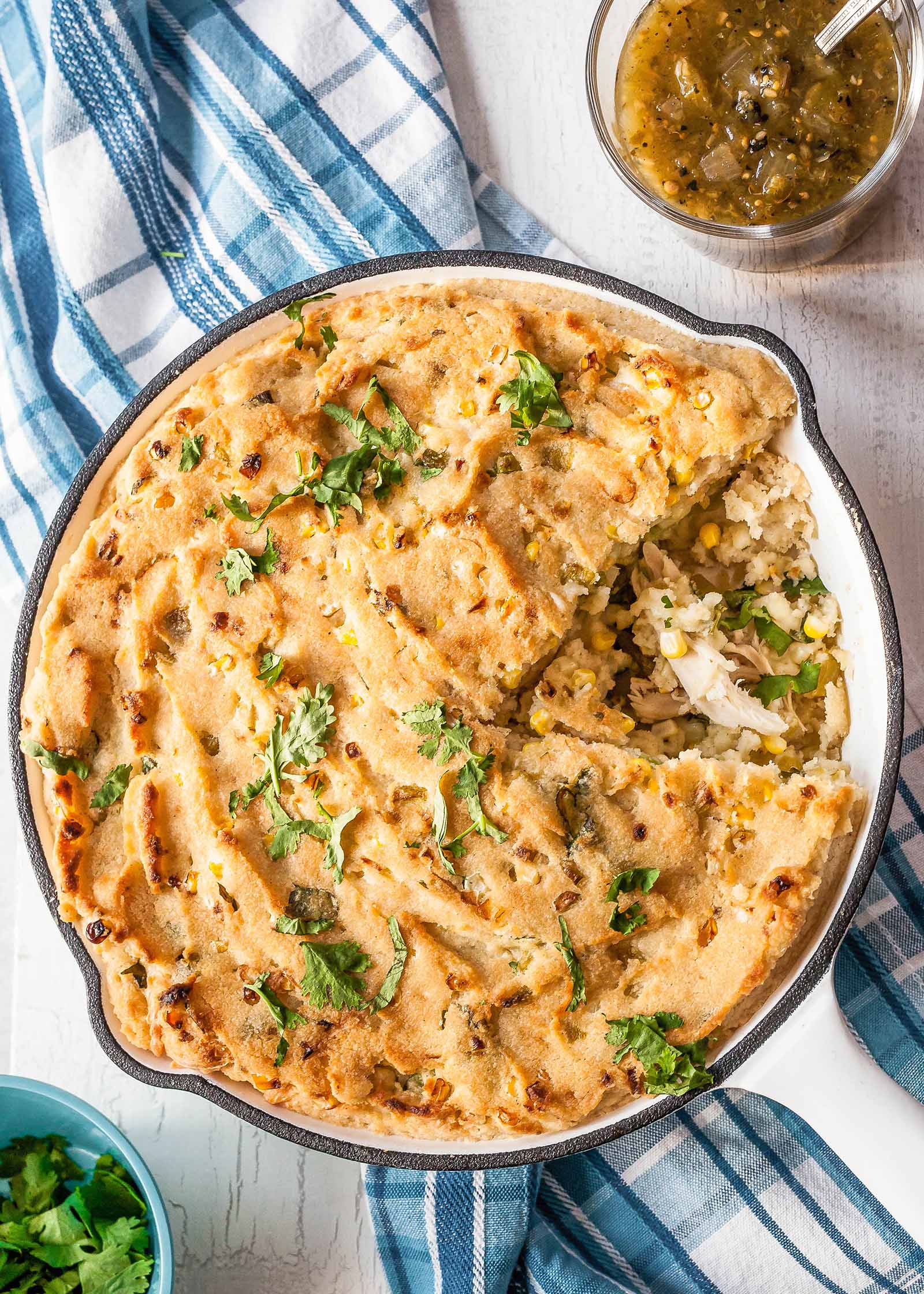 The best tamale pie casserole wtih rostisserie chicken in a white skillet on a blue plate linen with a slice taken out.