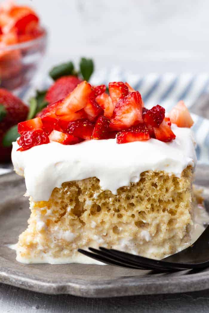 A slice of tres leches cake on a pewter plate, cake is topped with strawberries