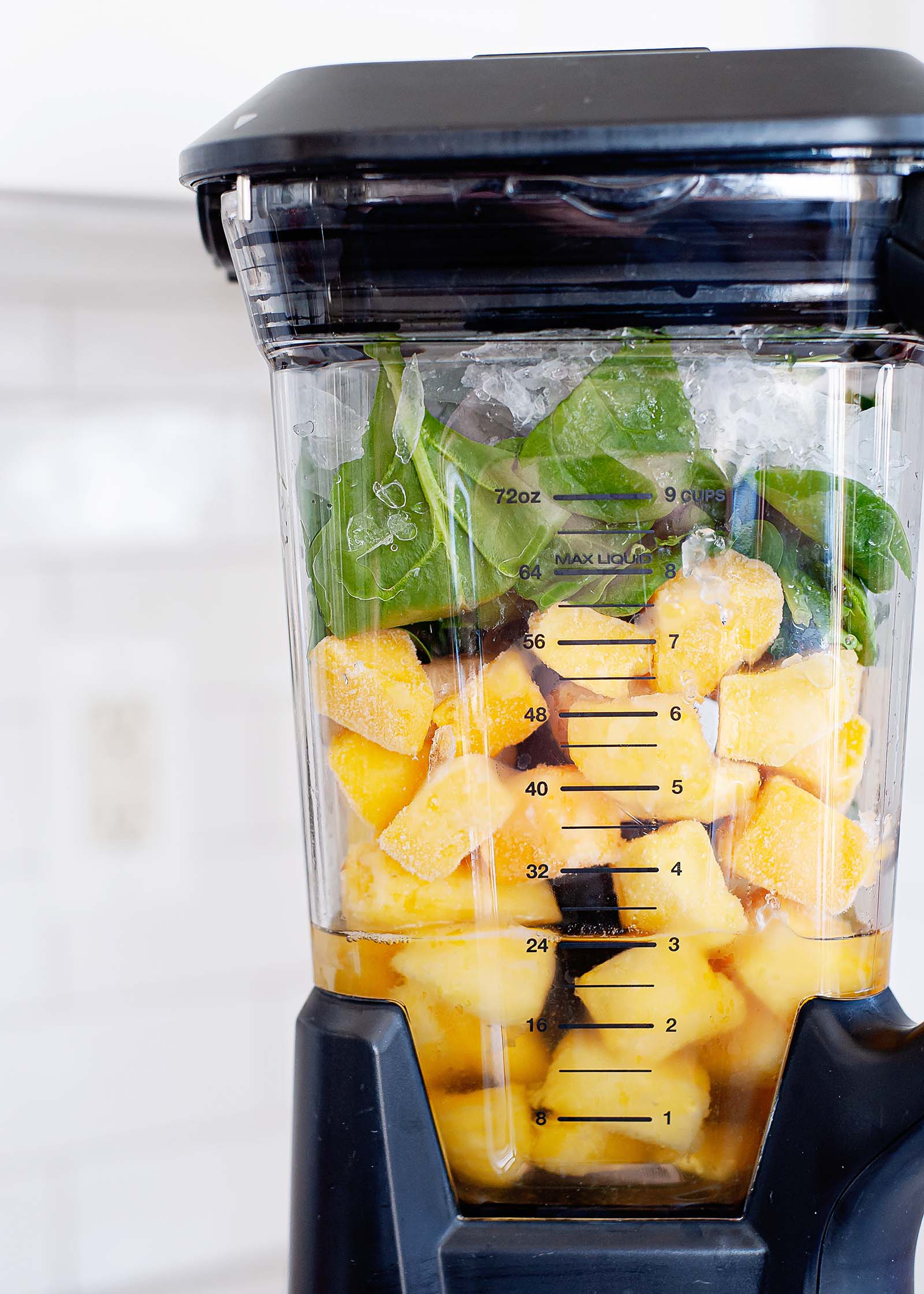 Close up view of a high speed blender jar with pineapple and spinach inside.