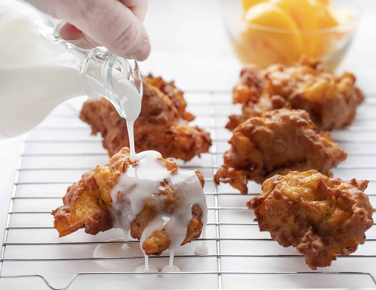 Le frittelle di pesca sono fatte con una pasta di cakey incorporata con pesche e condita con una glassa al gusto di pesca. frittelle di pesche, ricette di frittelle, glassa fatta in casa, sono un fornaio, iambaker, pasta fritta, frittelle di frutta Versare la glassa sulle frittelle di pesca