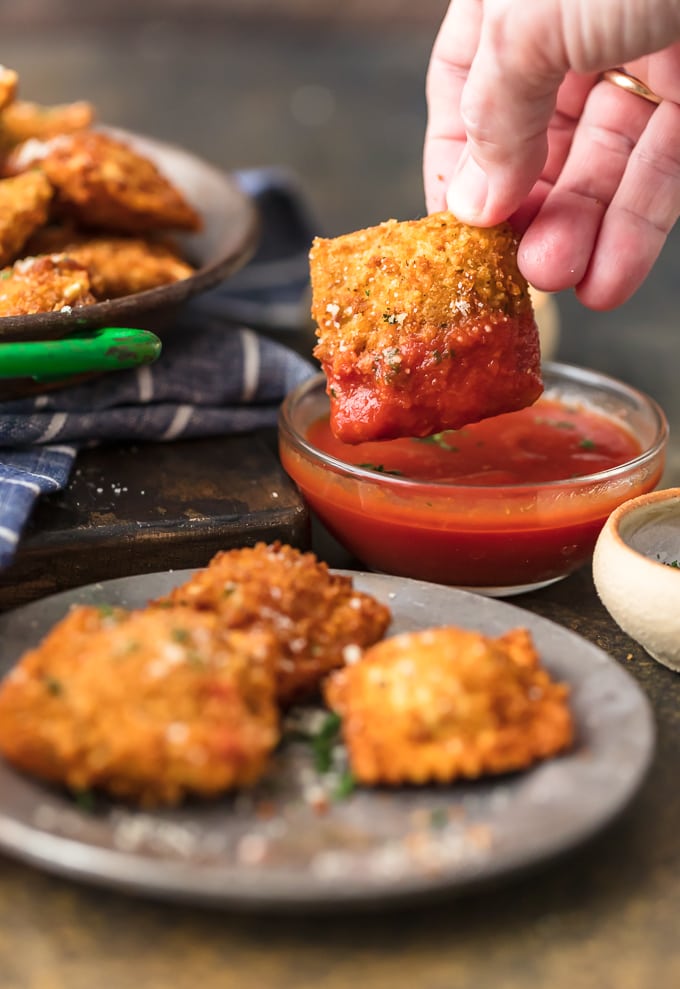 piatto di ravioli tostati in primo piano, immergendo uno dei ravioli in una piccola ciotola con salsa marinara