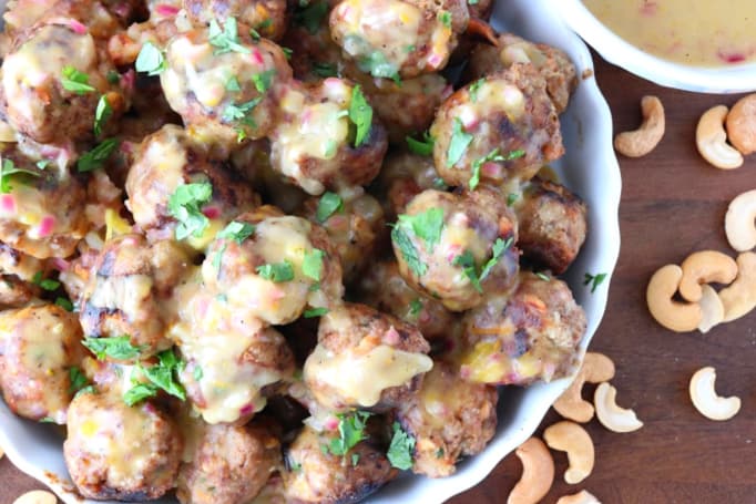 Foto del primo piano delle polpette di tacchino su un piatto con salsa, coriandolo tritato e anacardi dal lato.