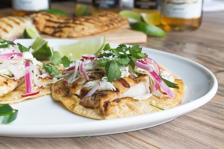 Tacos di pesce alla griglia marinati alla birra, questi classici tacos sono conditi con cavolo grattugiato, ravanelli, cipolle rosse in salamoia, fette di jalapeño e formaggio cojita.