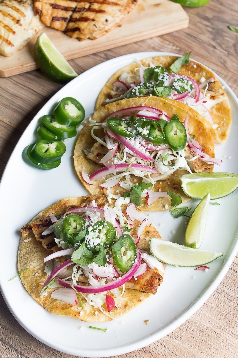 Tacos di pesce alla griglia marinati nella birra, questi classici tacos sono conditi con cavolo grattugiato, ravanelli, cipolle rosse sottaceto, fette di jalapeño e formaggio cojita.