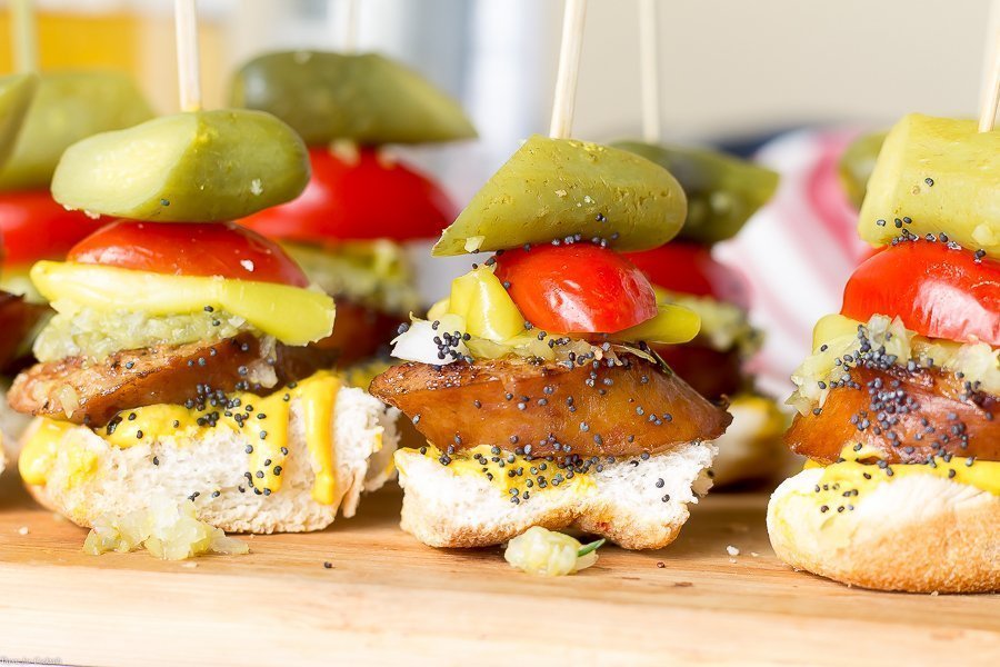 toast, spessa fetta di salsiccia affumicata, condimento dolce, cipolla bianca, senape gialla, lancia sottaceto, semi di sesamo, tutto in un boccone su uno spiedino, primo piano orizzontale