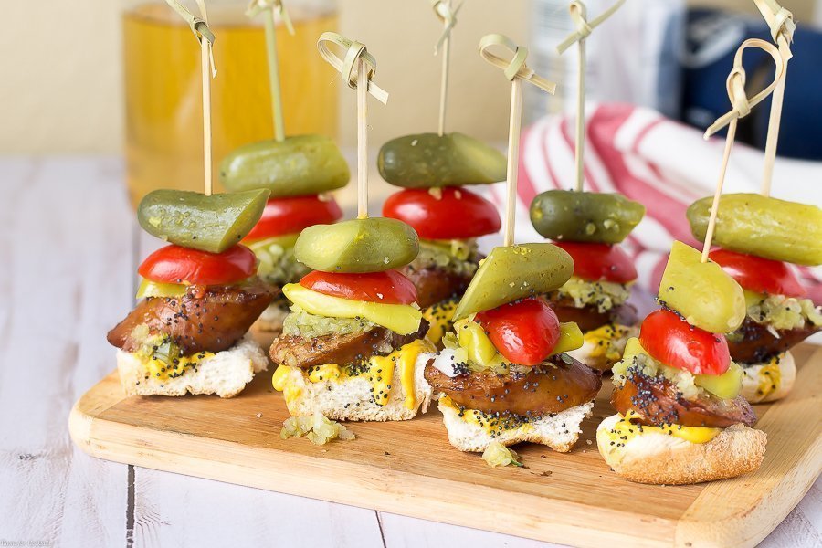 toast, spessa fetta di salsiccia affumicata, condimento dolce, cipolla bianca, senape gialla, lancia sottaceto, semi di sesamo, tutto in un boccone su uno spiedino
