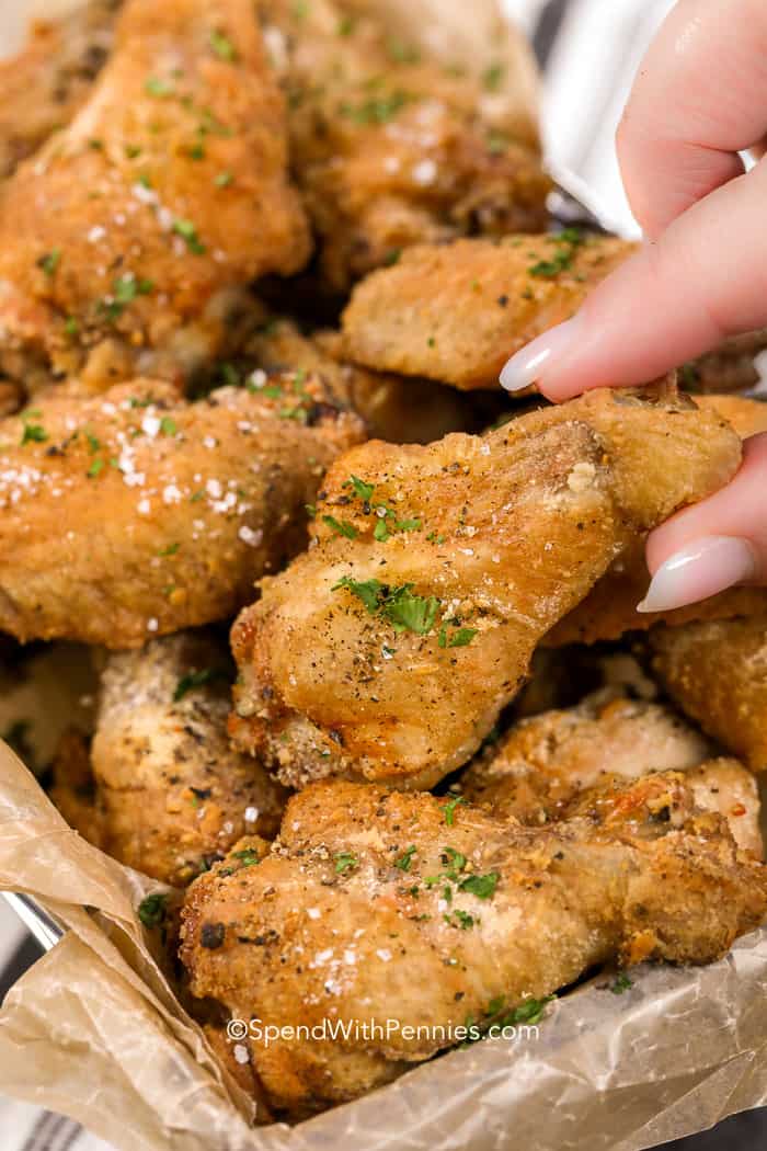 Una mano agarrando una freidora de aire ala de pollo para disfrutar.