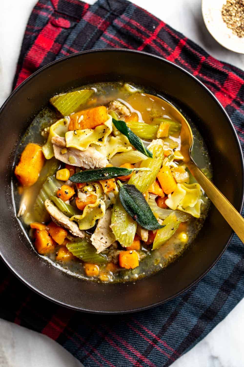 Cucchiaio d'oro in una ciotola di zuppa di noodle di tacchino con salvia croccante