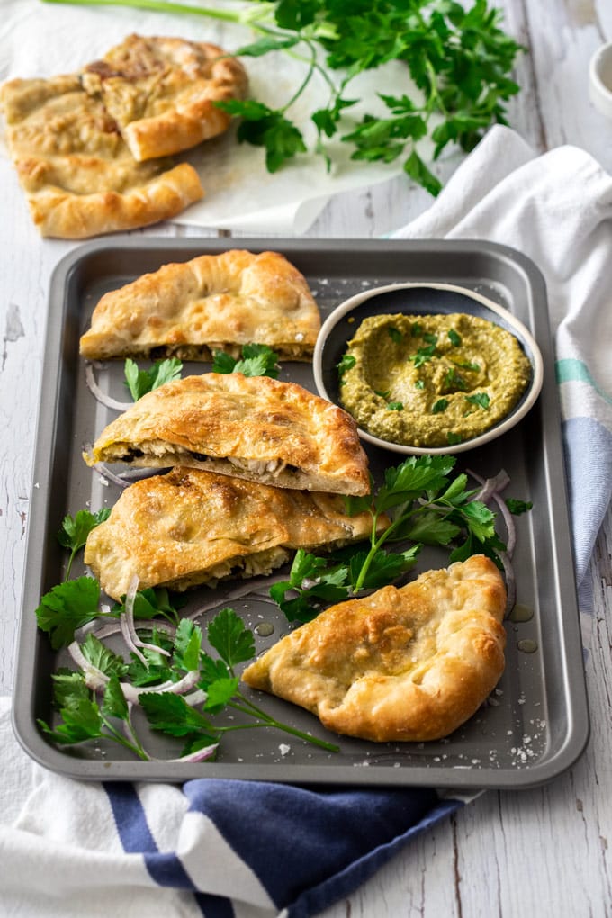 Fette di pollo pesto calzone su una teglia grigia circondata da prezzemolo e cipolla