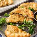 Fette di Calzone su una teglia grigia circondata da prezzemolo e cipolla.